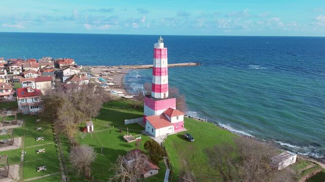 Camera orbits around iconic lighthouse, white with red stripes, perched atop rocky hill
