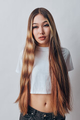 Young woman with long straight hair wearing white cropped t shirt standing against neutral background. Casual style, natural look, beauty and confident pose in studio.