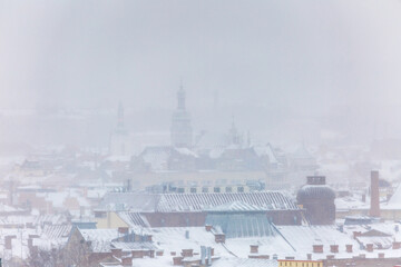 Fototapeta premium Distant view of Bernardine Monastery and St. Andrew's Church in Lviv during winter snowstorm. Scenic urban landscape of old town landmarks through thick fog and snowfall on cold January day.