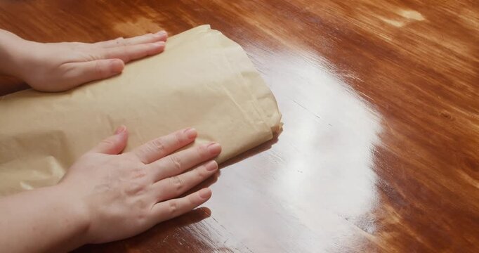 Woman wraps salmon fillet seasoned with salt and pepper in parchment paper for curing. Close-up of homemade salmon preparation process in kitchen, traditional food preservation and cooking at home.