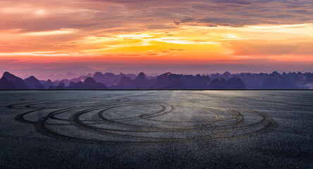 Obraz premium An empty asphalt race track with tire tracks and a beautiful mountain landscape under a dramatic sunset sky in Guilin