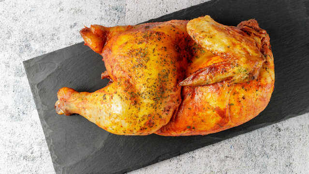 Baked grilled marinated in tomato sauce with herbs half of chicken on black stone board. Roasted chicken.