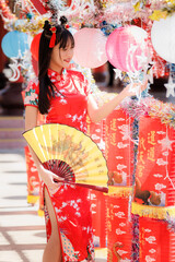 Naklejka premium Elegant young Asian woman in a red cheongsam holds a fan during a Lunar New Year celebration with lanterns