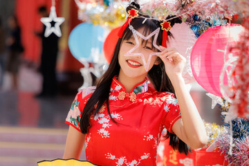 Happy young Asian woman in a red cheongsam celebrates Lunar New Year holding a star ornament amid...
