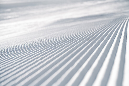 Corduroy snow texture on a freshly groomed ski slope, showing clean parallel ridges and detailed winter snow structure, ideal as background or texture for winter sports themes.