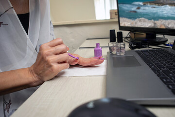 Woman working and doing manicure on work desk with laptop computer next to hands
