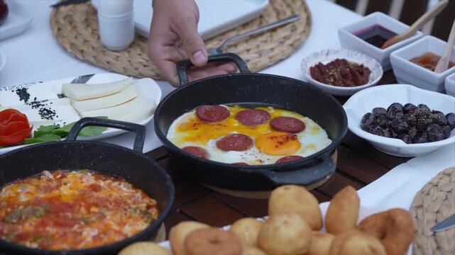Hand serving traditional Turkish breakfast with fried eggs and sucuk sausage on a table