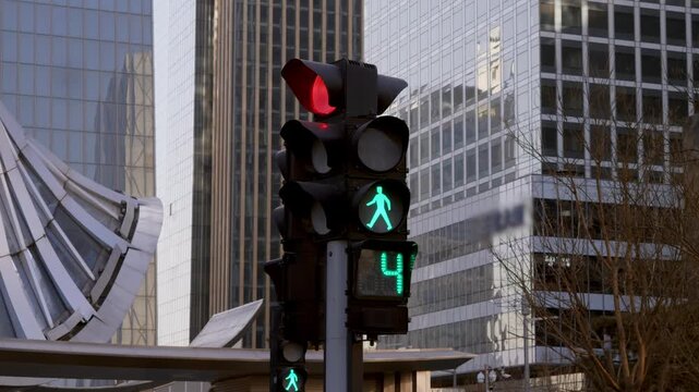 Close up urban shot shows pedestrian traffic light with green walking man and countdown timer reaching last seconds, then green signal ends and red stop light turns on.