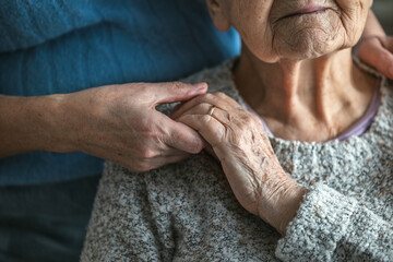 Elderly woman holding hands with her caregiver in a nursing home, close-up