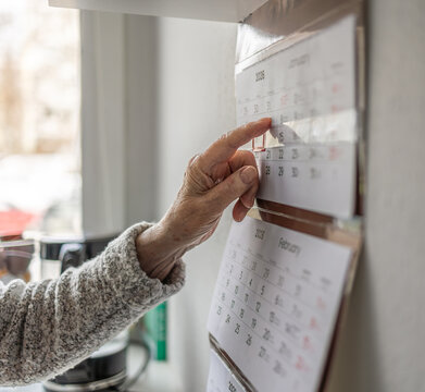Senior woman using a wall calendar in her kitchen, focus on finger
