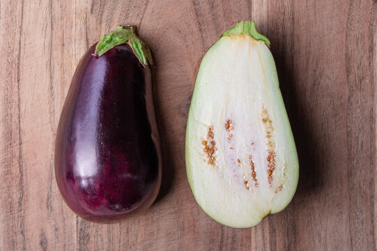 An eggplant cut in half showing inside and outside on wood cutting board