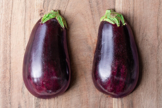 The exterior of an eggplant cut in half, two halves on wood cutting board