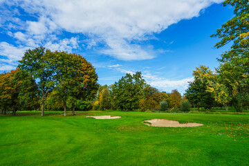 Obraz premium a professional golf course fairway featuring well-maintained sand traps and lush green grass. Beautiful autumn foliage on surrounding trees creates a peaceful outdoor sports atmosphere