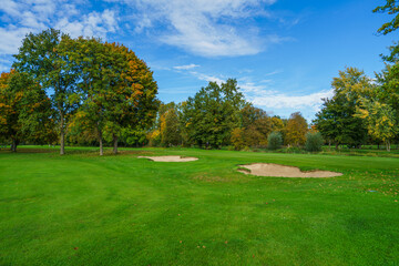 Obraz premium a professional golf course fairway featuring well-maintained sand traps and lush green grass. Beautiful autumn foliage on surrounding trees creates a peaceful outdoor sports atmosphere