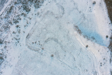 Fototapeta premium Winter field texture with snow and dry bushes in frost aerial top view