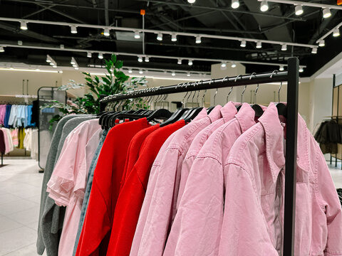 Pink denim jackets and red women's sweatshirts on hangers in a clothing store