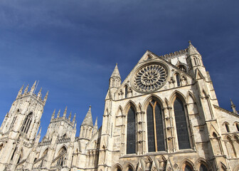 Fototapeta premium York Minster cathedral in York, England, showcasing Gothic architecture, towering spires, and an ornate rose window beneath a deep blue sky.