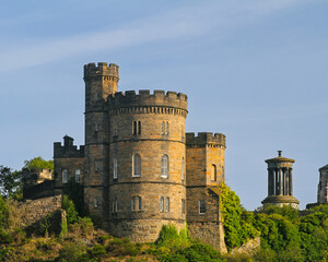 Historic stone tower on Calton Hill in Edinburgh, Scotland, with classical monuments and lush greenery under a clear blue sky.