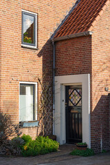 Red brick house with a black door and garden in the front.