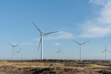 Wind turbines stand against the sky in a rural countryside.