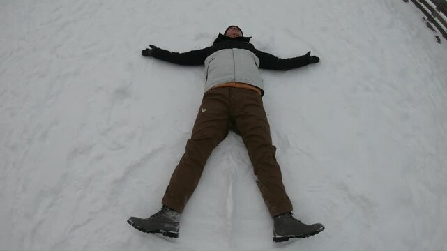 A joyful individual lies in freshly fallen snow, creating a snow angel with extended arms and legs.