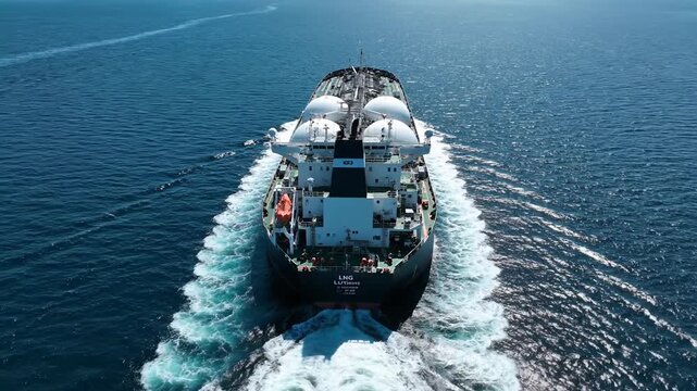 Aerial view of an LNG tanker ship sailing on the blue ocean, leaving a white wake.
