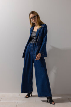 Elegant modern woman wearing oversized denim blazer and wide leg jeans with leather top, posing confidently in minimalist studio. Fashion, lifestyle, business casual concept with copy space.