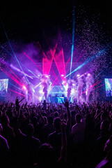 Exciting music festival crowd cheering during a live concert performance with vibrant lasers, confetti, and smoke. High-energy nightlife and entertainment event concept.