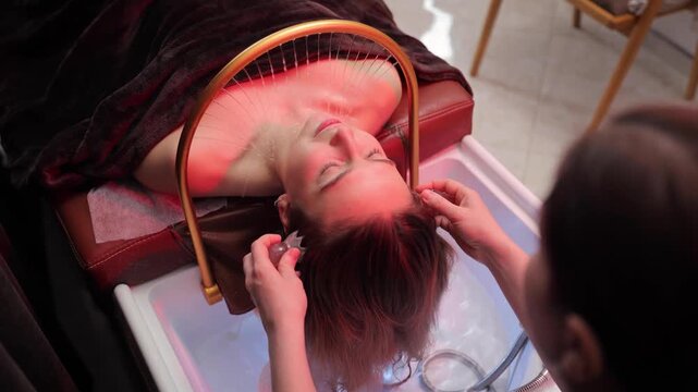 Client enjoying professional head massage and hair care therapy at beauty salon spa with specialized equipment and red light. Japanese head spa relaxation treatment