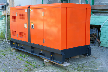 Outdoor industrial generator with orange casing on concrete blocks near brick wall