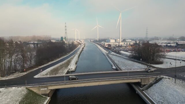 Halle, Vlaams Brabant, Belgium, 13th of January, 2026, Aerial winter view of canal and highway with wind turbines and industrial buildings in snowy landscape