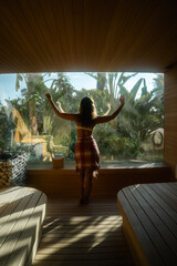 Serene Retreat: A woman stands with arms outstretched, experiencing the revitalizing bliss of a spa sanctuary, while a serene garden panorama unfolds beyond.