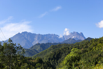 A high-angle view of Mount Kinabalu&rsquo;s rocky peaks towering over a dense tropical forest canopy under a clear blue sky in Sabah, Malaysia.