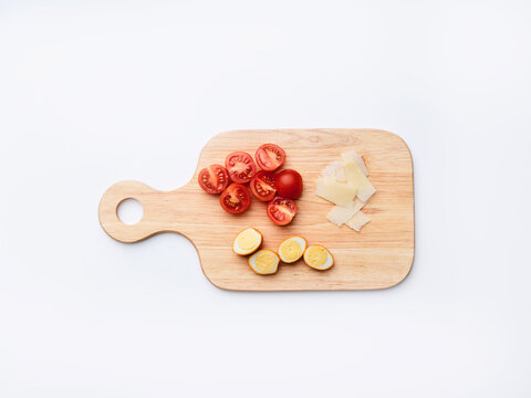 On a wooden cutting board, red cherry tomatoes, yellow citrus slices, and pieces of cheese are neatly arranged. This scene shows preparation for a meal and simple cooking tasks