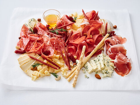 A large platter holds various cured meats, cheeses, nuts, and a small dish of honey. The spread is arranged neatly, showing different textures and shapes