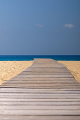 View of a wooden pathway stretching across soft sand towards the open beach of Mylopotas in Ios Greece 