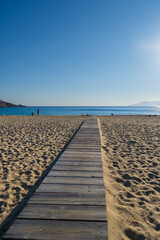 View of a wooden pathway stretching across soft sand towards the open beach of Mylopotas in Ios Greece 