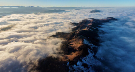 Fototapeta premium Breathtaking aerial view of mountain ridge piercing through sea of clouds. Sunlight illuminates patches of ridge. Distant mountain ranges create serene and expansive horizon.