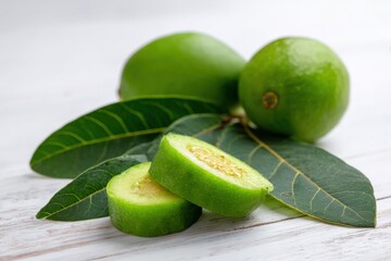 Obraz premium Fresh green guava slices and whole guavas with leaves on wooden surface