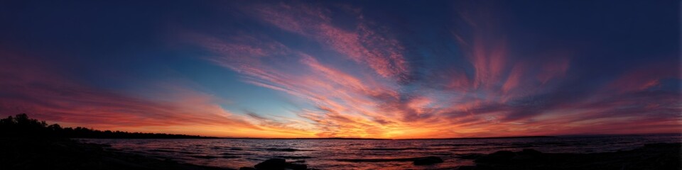 Obraz premium Breathtaking sunset over serene lake with vivid colors and dramatic clouds