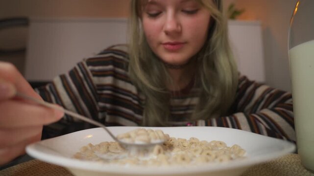 Close-up of teen girl with green hair eating cereal with fresh milk from white bowl with spoon, enjoy healthy and nutritious breakfast at home in cozy kitchen