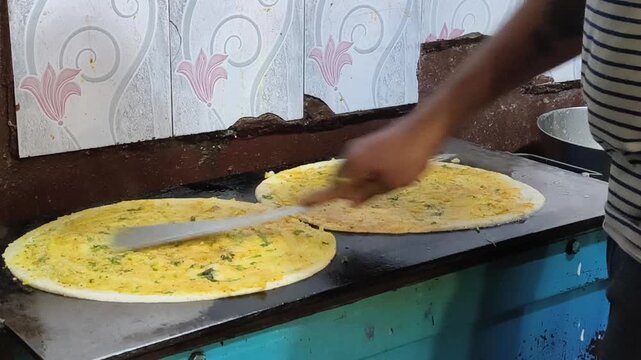 Two dosas cooking side by side on a large iron tawa at a street food stall. Shows authentic South Indian street food preparation.
