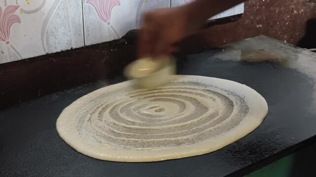 Plain dosa batter spread in a circular spiral on a hot tawa. Shows classic South Indian cooking technique and food preparation process.