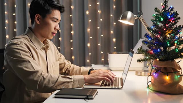 Man works on laptop near christmas tree at home during holiday