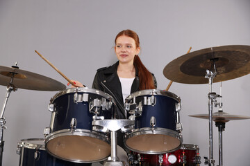 Teenage girl with drumsticks and drums on light grey background
