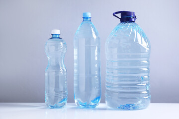 Naklejka premium Water bottles of different sizes on white table against grey background