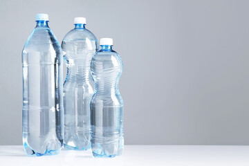 Fototapeta premium Water bottles of different sizes on white table against grey background, space for text