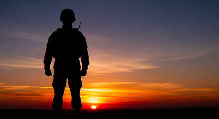 Fototapeta premium Silhouette of a soldier standing at attention against a vibrant sunset sky on the horizon