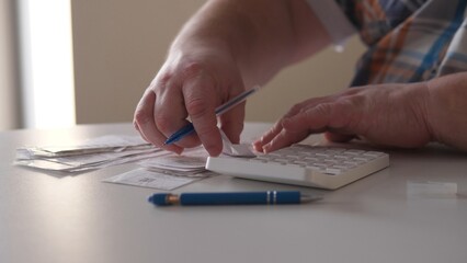 A person uses a calculator while holding a pen and arranging papers on a desk in a bright room. The workspace appears organized with items laid out for tasks.