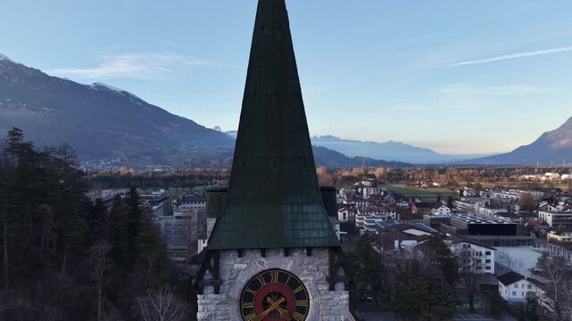 Ascending drone shot from a church clock tower up to the cross on the roof, birds flying away as the drone rises, with the Liechtenstein landscape visible in the background.